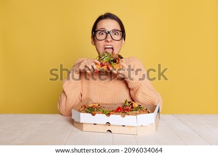 Excited young beautiful girl eating delicious pizza with cheese and tomatoes isolated on yellow studio background. World pizza day concept. Traditions, national food, popularity, taste. Copy space for