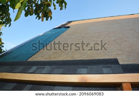New roofing construction and asphalt shingles installation. A close-up of asphalt shingles installation on plywood, osb roof sheathing and waterproofing roof underlayment. Royalty-Free Stock Photo #2096069083
