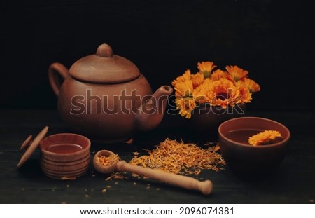 Herbal tea in a cup and teapot made of fresh and dried calendula flowers with honey on a dark wood background.