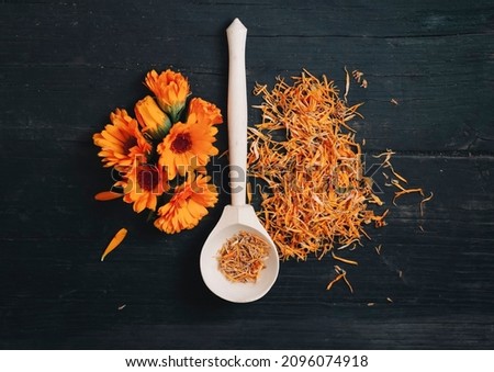 bright fresh flowers and dried calendula flowers with a spoon on a black wooden background top view..