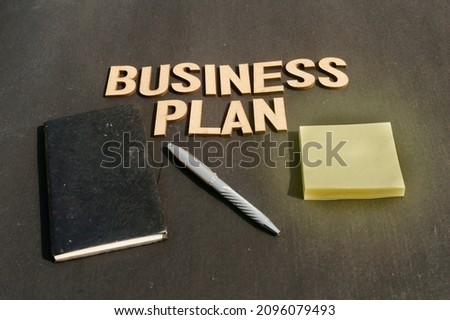 Businessman hand placing a pen and notebook in front of Word Business Plan made of wooden blocks of Alphabet letters. High Angle View. Vertical background. Close up