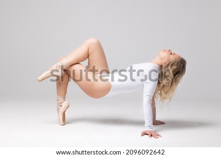 Ballerina, blonde in a white training leotard posing on the floor in pointe shoes.
