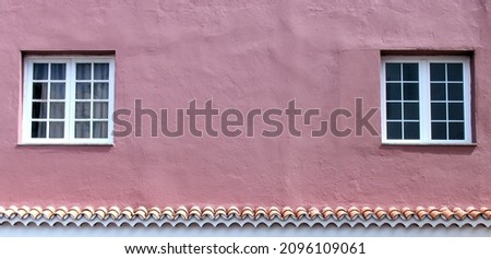 An old weathered pink concrete wall of a house with two wooden windows