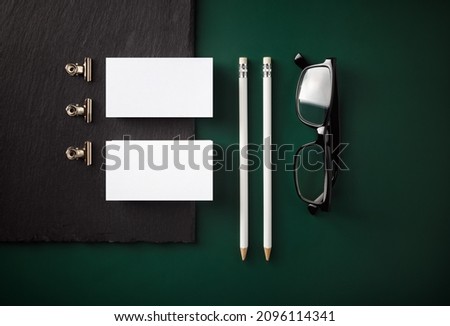 Photo of blank business cards, pencils and glasses on green background. Flat lay.
