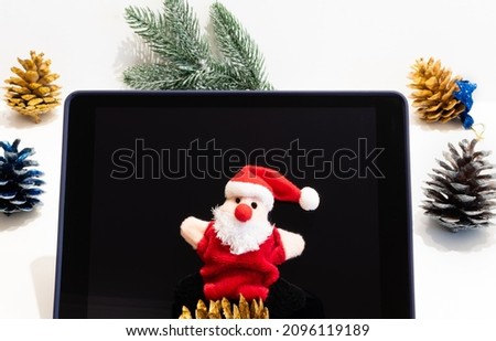 Funny Santa Claus toy on tablet on blurred background of New Year decorations on white table