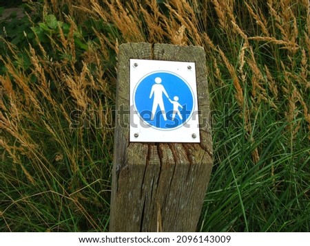 Dutch pedestrian information traffic board sign of footpath in park dunes showing the way public should use to walk on a piece of wood pole post with green grass and dry grass in Holland, The Hague