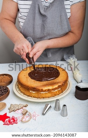 Woman hands chef spreading cream on second layer of Chocolate cake. Making Chocolate Layer Cake.  Christmas cake on the kitchen table.