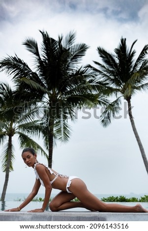 A Thai model with tan skin and white bikini posting on swimming pool at Koh Samui, Thailand.
