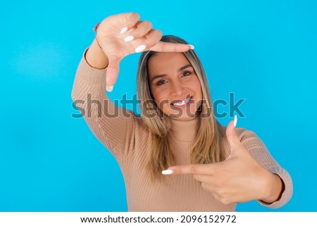 Young hispanic girl wearing turtleneck over blue background  making finger frame with hands. Creativity and photography concept.