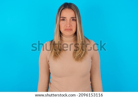 Displeased upset Young hispanic girl wearing turtleneck over blue background  frowns face as going to cry, being discontent and unhappy as can't achieve goals,  Disappointed model has troubles