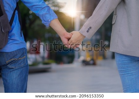 Close-up of a loving couple holding hands while walking on the street with back view with front lighting.