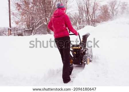 A girl in a red jacket cleans the snow with a snow blower.
