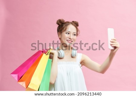Beautiful girl holding shopping bags and taking selfie with cell phone isolated on pink background