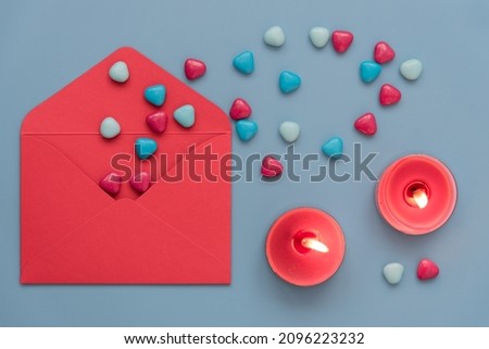 A stylish and cozy picture for Valentine's Day. View from above, on a blue background laid out an envelope, candles and hearts. A red envelope from which hearts are poured. Burning candles create a