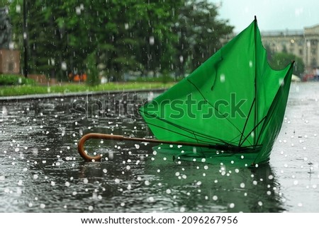 Broken green umbrella in park on rainy day with hail