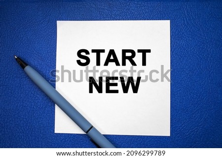 New start is written on a white sheet of paper which lies on a blue textured background with a pen.