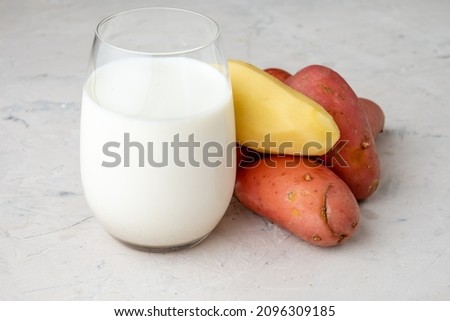 Vegan milk from potatoes in a glass next to the potato tubers. White table.