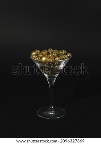 Golden Christmas baubles decoration in martini glass on black background. New year or Christmas Eve party concept.