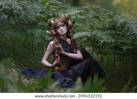 Red-haired girl with moss-covered horns sits among the ferns in the forest