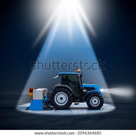 Side view of a new tractor and a resurfacer maintenance machine polishing a big ice field into a skating rink in the night in the spotlight with copy space