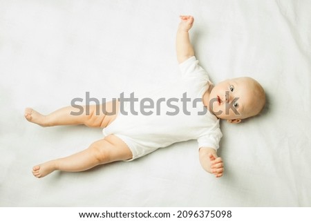 Little baby in a white dress lying on her back on a white sheet. Flat lay, top view.