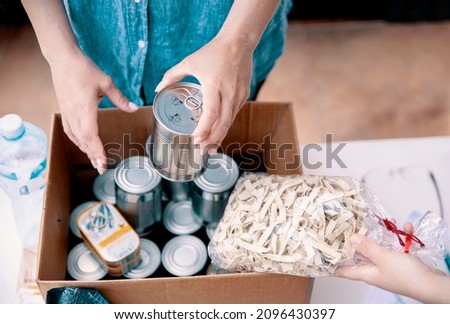 Volunteer hands collecting food into donation box. Working at food bank concept. Cut out middle section image of hands packing Cans at Food Drive Royalty-Free Stock Photo #2096430397