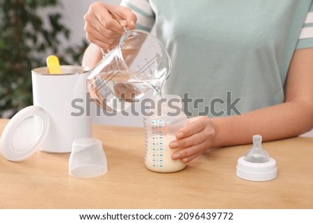 Woman preparing infant formula at table indoors, closeup. Baby milk Royalty-Free Stock Photo #2096439772