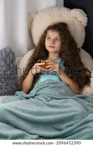 Little girl is drinking tea under the blanket