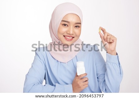 Hempseed oil softgel capsule supplement. Smiling asian hijab girl taking Hempseed oil Capsule with white plastic bottle Royalty-Free Stock Photo #2096453797