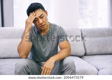Feeling stressed. Frustrated handsome young man touching his head and keeping eyes closed while sitting on the couch at home Royalty-Free Stock Photo #2096473579