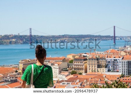 A young girl with a green dress staring at the Lisbon skyline from a viewpoint. Lisbon, Portugal.