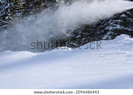 Snow making machine at a Rocky Mountain ski resort. Snow covered pine trees in the background with fresh natural and created snow below.