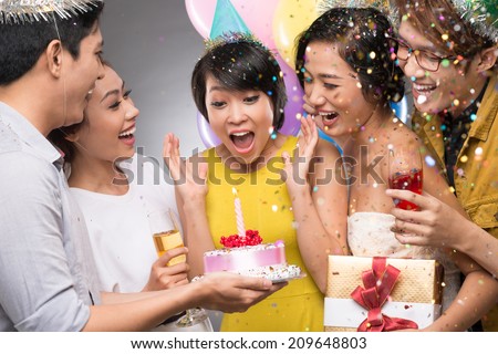Friends presenting a birthday cake to the astonished girl