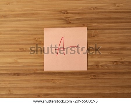 Sticker depicting the letter a. Paper sticker pasted on a wooden surface. Self-adhesive paper sheet. A piece of paper on a wooden board. Reminder for action. Paper sheet for notes.