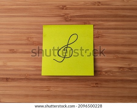 Sticker depicting the treble clef symbol. Paper sticker pasted on a wooden surface. Self-adhesive paper sheet. A piece of paper on a wooden board. Reminder for action. Paper sheet for notes.