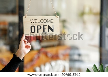 Open. barista, waitress woman wearing protection face mask turning open signboard on the glass door in modern cafe coffee shop, cafe-restaurant, retail store, small business owner, food and drink conc