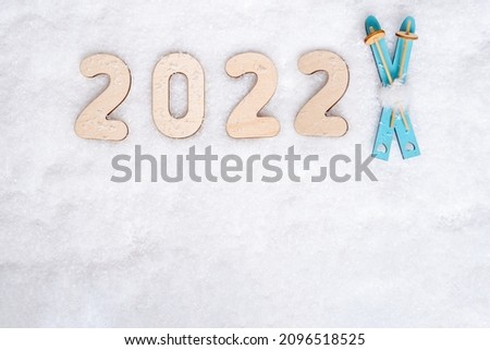 Sports year 2022. Bright blue wooden toys ski and date 2022 on white snow, flat lay, copy space. Love for skiing