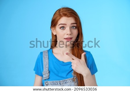 Curious redhead girl pointing left questioned, intrigued about interesting copy space look wondered ambushed camera, raise eyebrows confused, discuss product, stand blue background Royalty-Free Stock Photo #2096533036