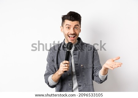 Handsome smiling performer talking in mic, gesturing and performing, making speech with microphone, standing against white background Royalty-Free Stock Photo #2096533105