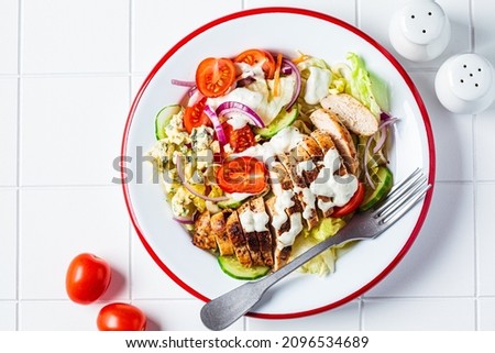 Buffalo chicken salad with gorgonzola cheese, tomato, cucumber and ranch dressing, white tile background, top view. Royalty-Free Stock Photo #2096534689