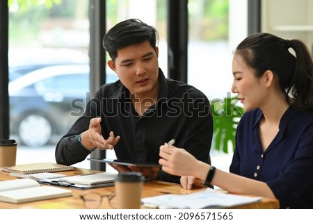 Photo of a young business development team working together at the wooden working desk surrounded by various office equipment.