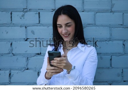 Young, pretty brunette woman is looking at her mobile phone. In the background a grey brick wall. Concept of new technologies and social networks. Royalty-Free Stock Photo #2096580265