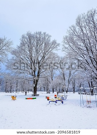 an empty park with a children's swing in the snow on a cold winter morning