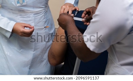 A nurse is just removing needle and syringe from an injection site on left arm of a patient, during Covid-19 vaccination event. A close-up and selective focus photo of syringe and nurse fingers.
