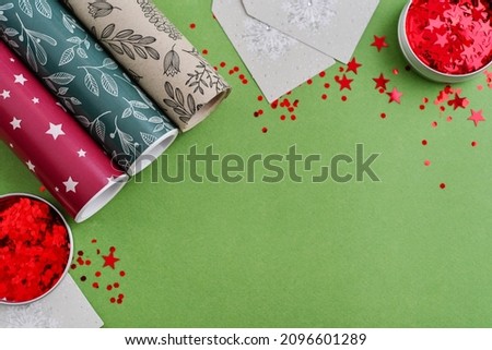 Rolls of colored wrapping paper with gift tags and  sparkle red confetti on green background, top view