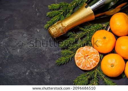 Christmas composition with tangerines and champagne bottle on black background, with green spruce tree branch.