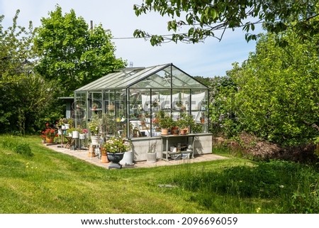Beautiful greenhouse glass house in the garden yard near the villa. There are lots of pots with blooming blossom colorful flowers. Landscape garden design. Greenhouse for growing plant seedlings. Royalty-Free Stock Photo #2096696059