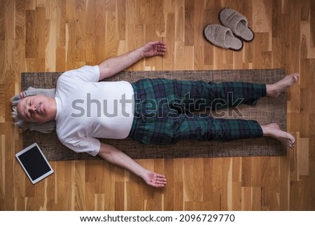 Senior man meditating on a wooden floor and lying in Shavasana pose. Royalty-Free Stock Photo #2096729770