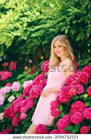 Outdoor portrait of young beautiful woman posing with hydrangea flowers in summer garden