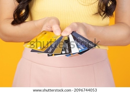 Close up hands young asian woman wearing t-shirt holding many bank card, credit card isolated on yellow background. Business online shopping concept.